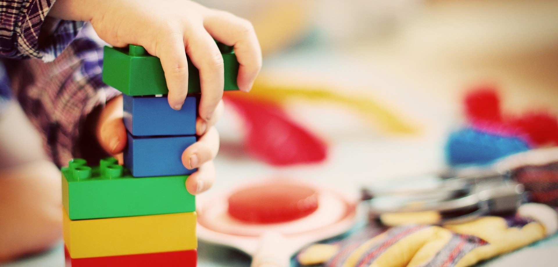 Das Bild zeigt die Hände eines Kindes, das mit bunten Legosteinen spielt und diese stapelt.