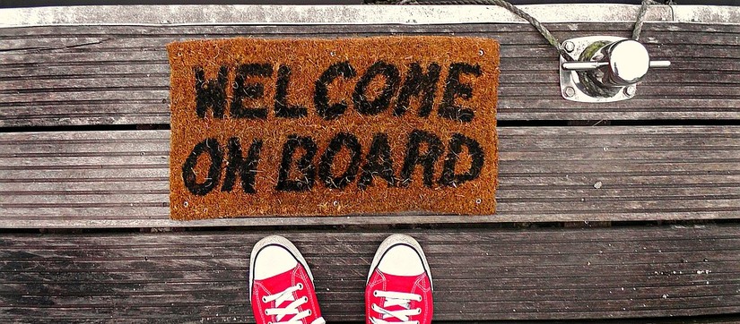 Das Bild zeigt ein paar Turnschuhe die vor einer Fußmatte mit dem Text "Welcome on board" steh