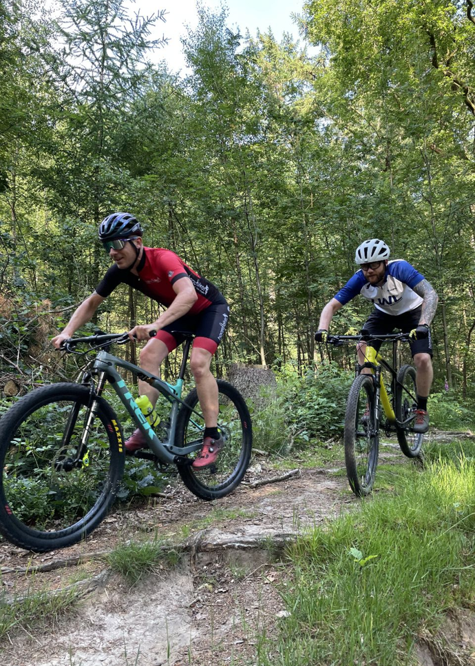 Das Bild zeigt zwei Mountainbike-Fahrer, die durch einen Wald fahren.