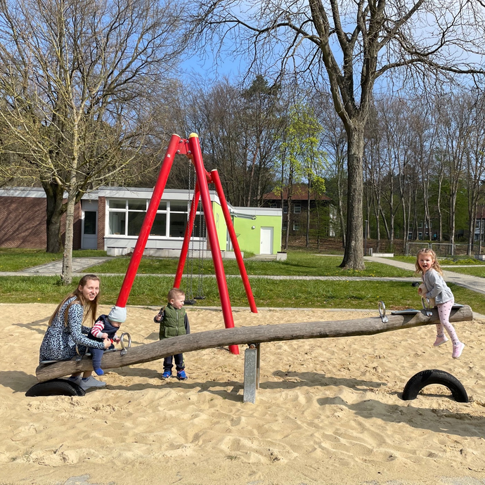 Das Bild zeigt eine Frau mit ihren drei Kindern auf einer Wippe auf einem Spielplatz. (öffnet vergrößerte Bildansicht)