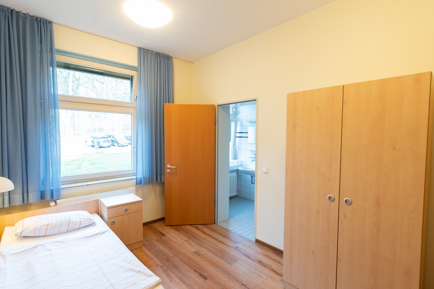 Das Bild zeigt ein Patientenzimmer, in dem unter anderem ein Bett und ein Schrank stehen.