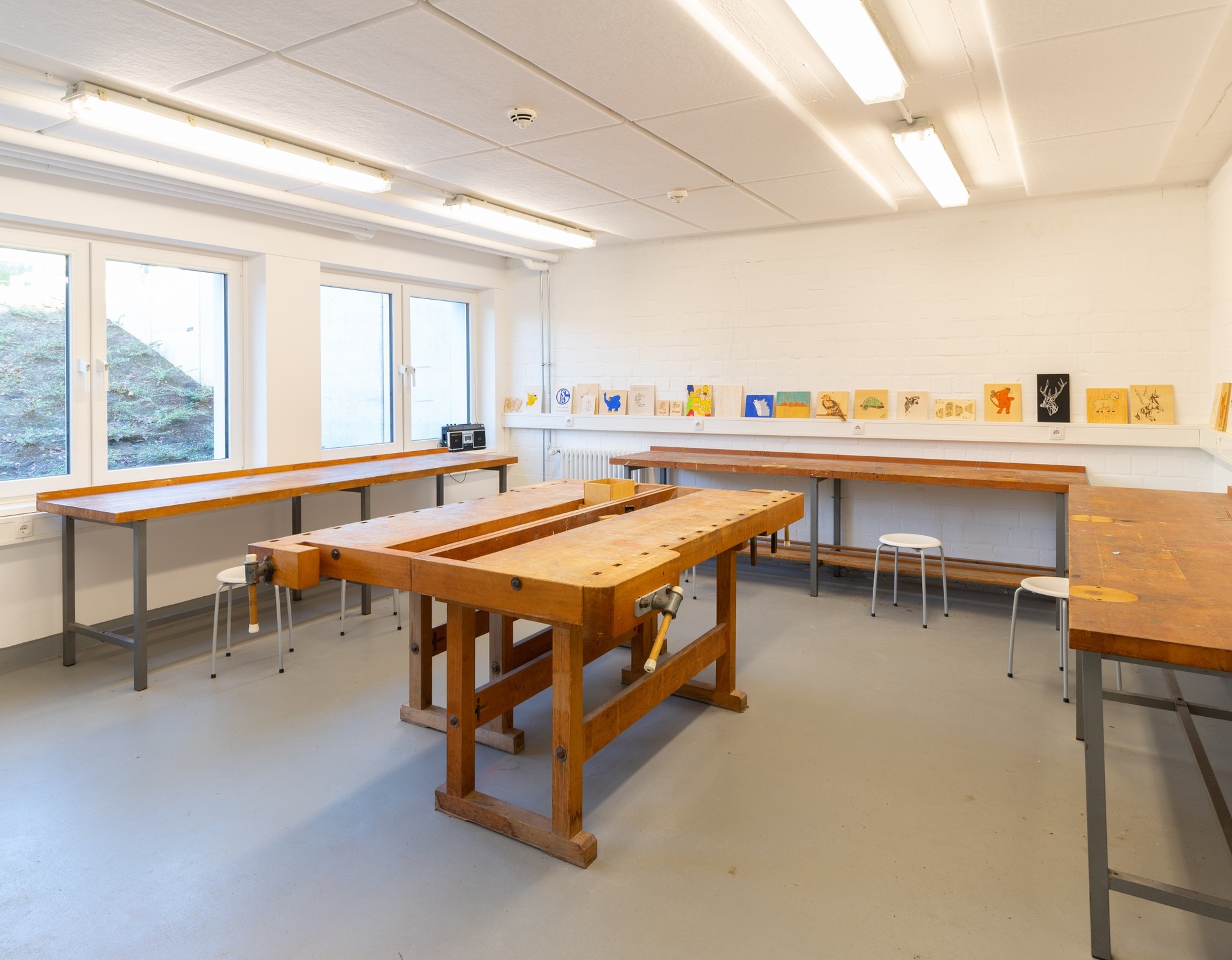 In dem Werkraum der Schule steht in der Mitte ein großer heller Holztisch. An den Wänden hängen hergestellte Bildwerke.