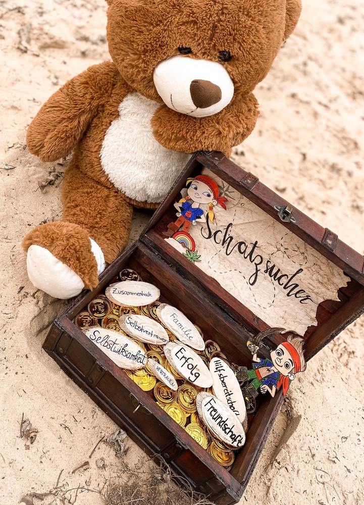 Das Bild zeigt einen Teddybär, der eine braune kleine Schatzkiste öffnet.