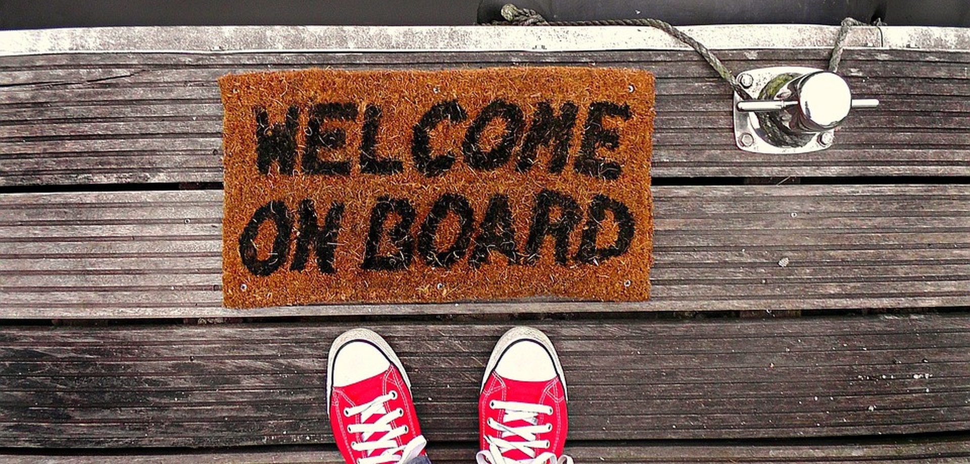 Das Bild zeigt ein paar Turnschuhe die vor einer Fußmatte mit dem Text "Welcome on board" stehen.