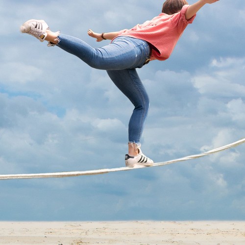 Das Bild zeigt ein Mädchen in einem rosa Sirt, das über ein gespanntes Seil balanciert.